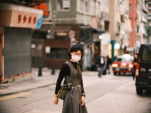 asian woman in specs and face mask crossing street in chinese city